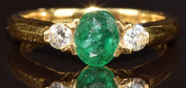 An 18ct gold ring set with an oval cut emerald of approximately 0.6ct and two round cut diamonds,