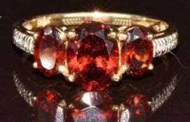 A 9k gold ring set with three oval cut Malaya garnets and zircons, total carat weight of garnets 2.