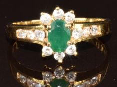 An 18ct gold ring set with an oval cut emerald of approximately 0.5ct surrounded by diamonds, 3.