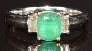 An 18k white gold ring set with a cushion shaped emerald of approximately 1ct and two baguette cut