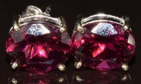 A pair of 9k white gold earrings each set with an oval cut magenta garnet of approximately 2.6ct,