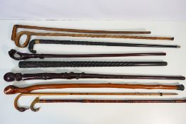 A collection of walking sticks, predominantly with carved decoration.