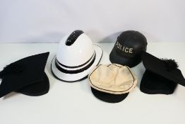 A vintage Cromwell fire helmet in white, two mortarboard academic caps and a mounted police helmet.