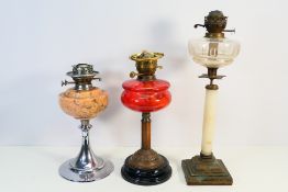 Three oil lamp bodies with glass oil fonts/bowls, one clear glass, one red and one marbled effect.