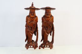 A pair of Chinese wooden carvings in the form of a man holding beads and a fly whisk,