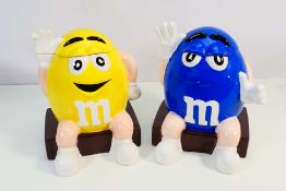Two M&M's novelty biscuit barrels, yellow and blue, approximately 26 cm (h).