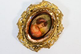 A yellow metal brooch with hand painted ceramic panel depicting a young lady below a faceted glass