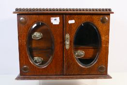 An oak smoker's cabinet with twin glazed doors opening to reveal three interior drawers,
