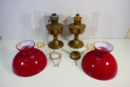 A pair of brass oil lamps with red glass shades, approximately 36 cm (h) excluding chimney.