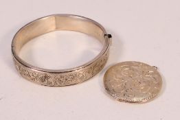 A silver locket pendant of circular form with engraved decoration and a silver hinged bangle.