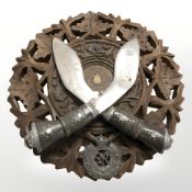 A decorative carved wooden circular plaque with two kukri knives, diameter 22 cm.