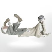 A Lladro figure of a recumbent clown with his foot resting on a ball.