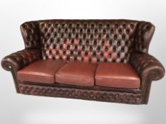 A Chesterfield style oxblood buttoned leather wingback three seater settee and matching armchair.