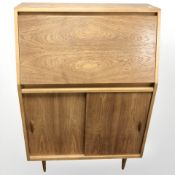A Jonelle teak fall front writing bureau with sliding cabinet doors beneath,
