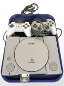 A Sony Playstation 1 console model SCPH-9002, with two controllers and leads.