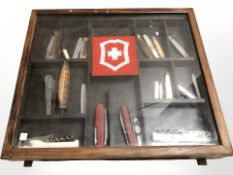 A counter top cabinet containing a collection of pocket knives, Swiss army knives, etc.