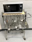 A Sharp microwave and a chrome kitchen trolley with utensils