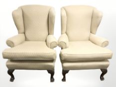 A pair of 20th century wingback armchairs on carved lion paw feet.