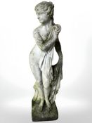 A weathered concrete garden statue in the form of a scantily clad maiden,