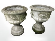 A pair of weathered concrete garden urns each with twin lion masks holding ring handles,