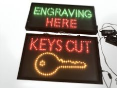 Two illuminated signs 'Engraving Here' and 'Keys Cut', width 60 cm.