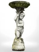 A weathered concrete garden bird bath held aloft by a cherub,