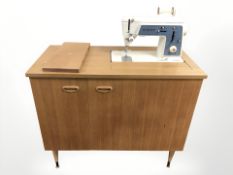 A Singer electric sewing machine in teak cabinet, width 89 cm.