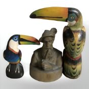 A black forest carving of a man smoking a pipe, and two carved and painted figures of toucans,