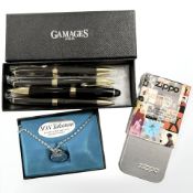 A group of Gamages ball point pens together with an Elvis Zippo lighter and a Talisman chain