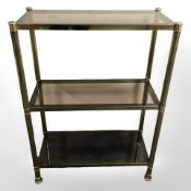 A brass and smoked glass three tier bookcase stand,