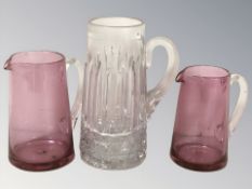 Two ruby glass jugs and a further clear jug, tallest 24 cm.