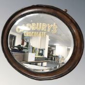 An Edwardian oval wall mirror with later Cadbury's chocolate advertising decoration, width 60 cm.