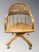 A reproduction oak spindle back swivel armchair, with caned backrest, width 60 cm.