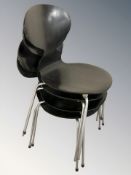 A set of four ebonised laminated wood stackable chairs on metal legs.