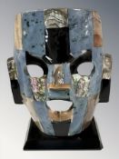 A Mexican polished hardstone inlaid burial mask ornament on ebonised plinth,