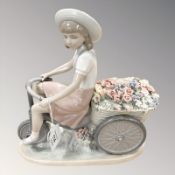 A Lladro figure of a girl riding a bike with flowers, height 26 cm.