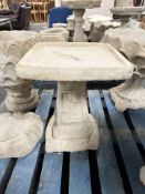 A concrete pedestal bird bath with ivy decoration.