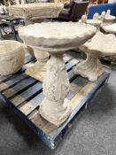 A concrete pedestal bird bath with ornate base.