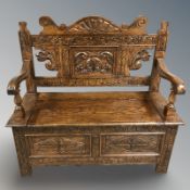 A reproduction heavily carved oak storage settle, 103 cm x 43 cm x 100 cm.