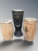 An African hide covered drum carved with a face, height 57 cm, and a further pair of drums.