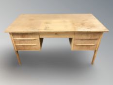 A 20th century Danish faded teak twin-pedestal writing desk, fitted with seven drawers,
