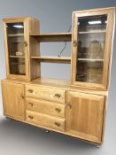 An Ercol light elm sideboard, with bookshelf and glazed cabinets above,