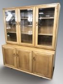 An Ercol light elm glazed triple door cabinet, fitted cupboards beneath, 137 cm x 45 cm x 161 cm.