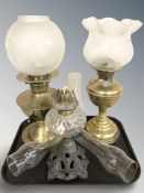 Two brass oil lamps with etched glass shades and a further cast patinated oil lamp with clear glass