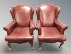 A pair of oxblood leather wing back armchairs on claw and ball feet,