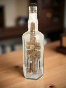 A folk art mining model in bottle, containing several hand tools and a wooden scaffold, signed WH,
