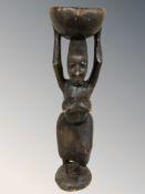 An African carved hardwood maternity statue modelled as a nude woman holding a bowl atop her head,
