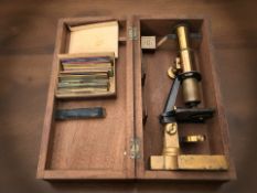 A lacquered brass microscope in case, glass slides, etc.