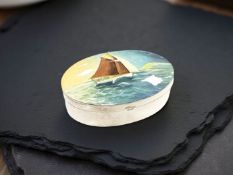 A silver oval lidded pot with hand painted enamel decoration depicting a sailing boat at sea,