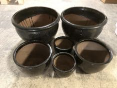 Two sets of three black glazed earthen ware garden planters,